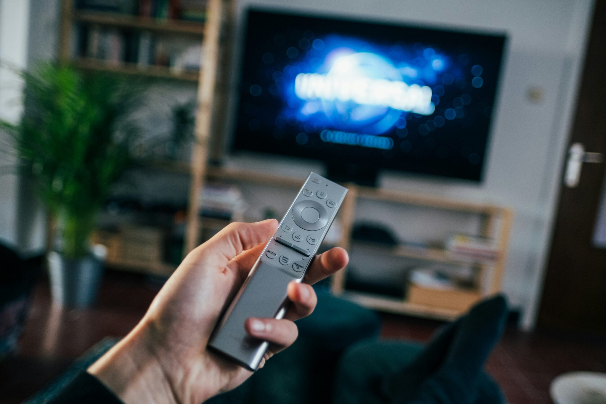 Mando de televisión en primer plano con un televisor de fondo